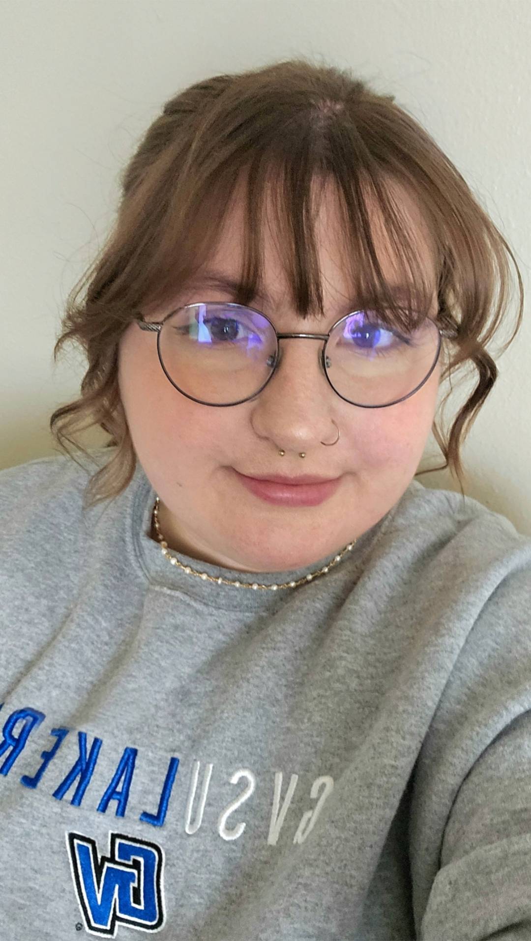 Girl with brown curly hair smiling at the camera. She has round glasses and is wearing a GVSU sweatshirt